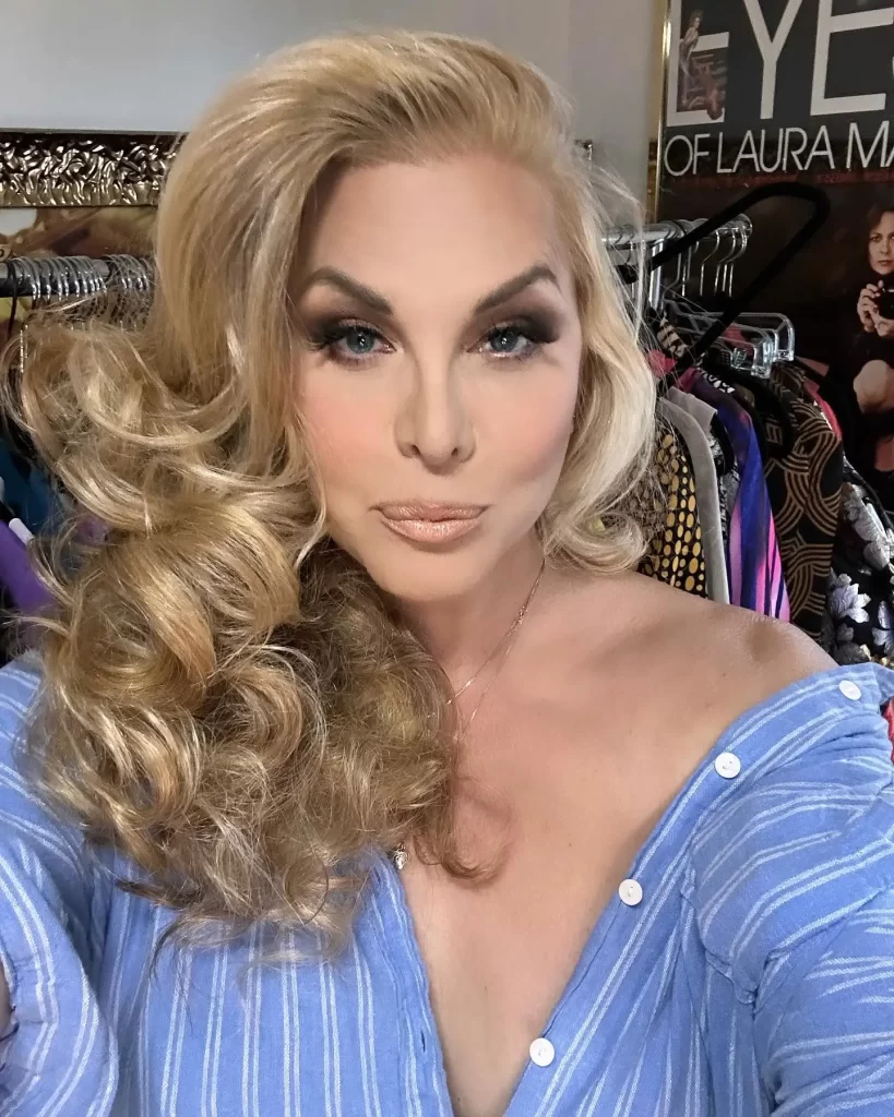 Candis Cayne with voluminous blonde hair, blue top, makeup.
