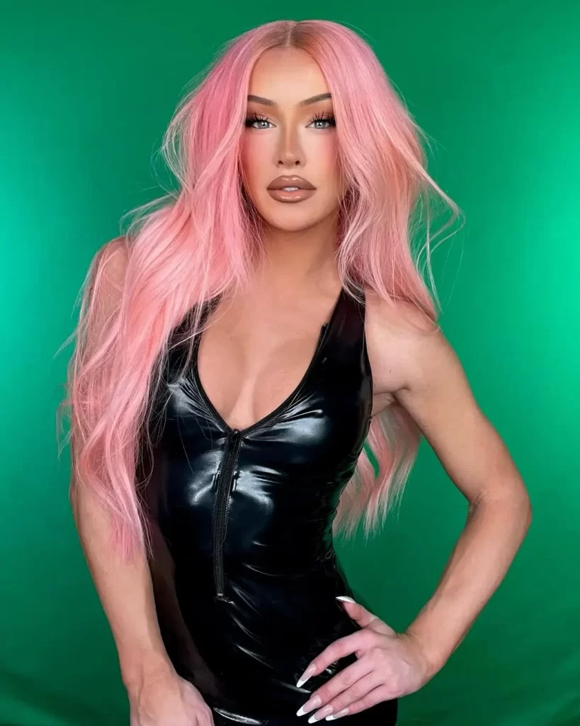 Gigi Gorgeous with pink hair, black dress, green background.