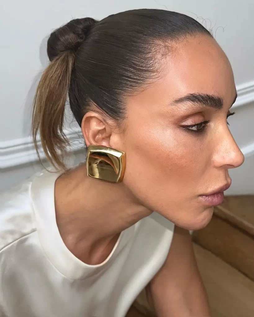 Ines Rau with sleek bun and gold earring.