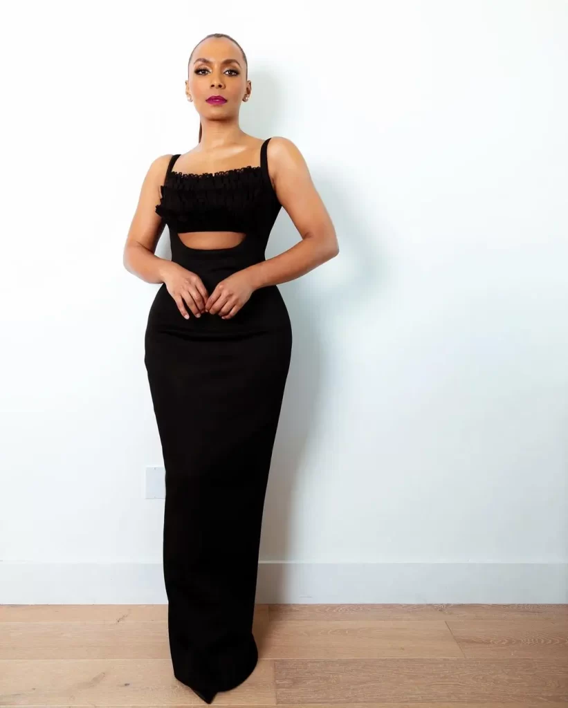 Janet Mock in elegant black dress posing against white background.