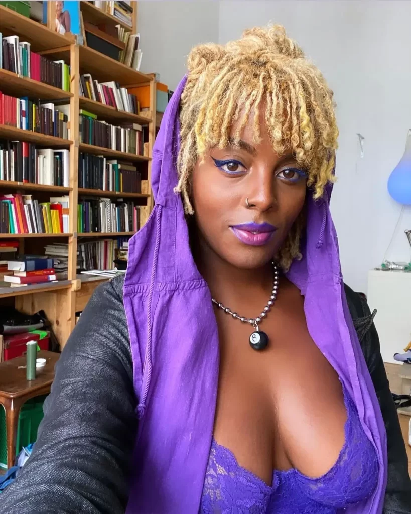 Juliana Huxtable with purple hoodie and lipstick indoors.