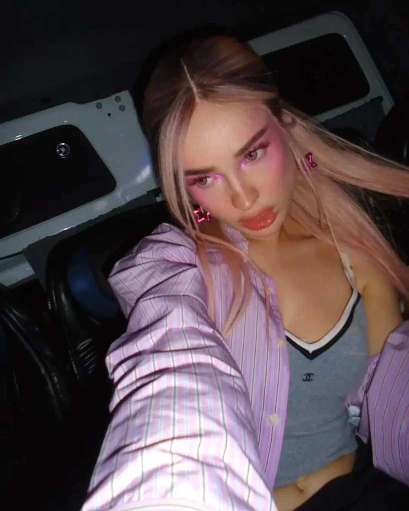 Kim Petras with pink hair in striped shirt, indoor lighting.