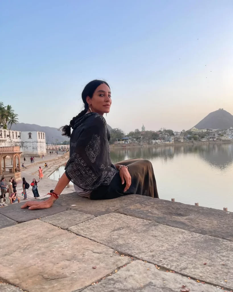 Lea T sitting by lakeside with mountain background.