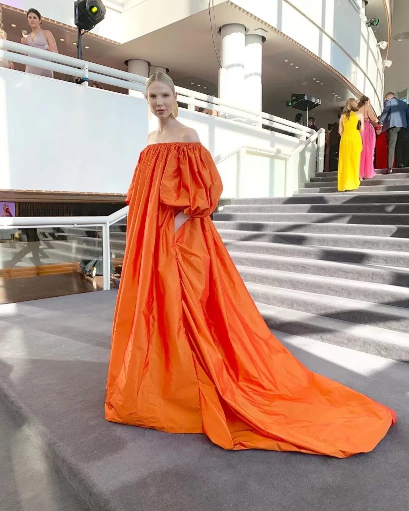 Valentijn De Hingh in vibrant orange gown on stairs.