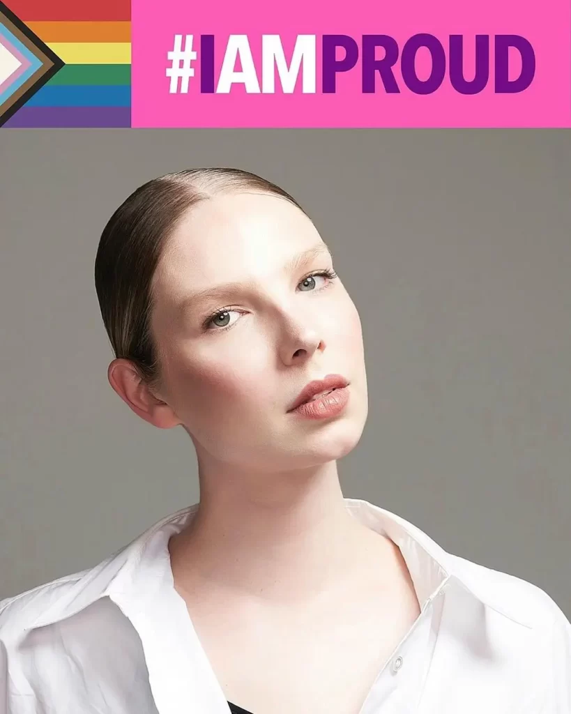 Valentijn De Hingh posing with #IAMProud sign, Pride colors in background