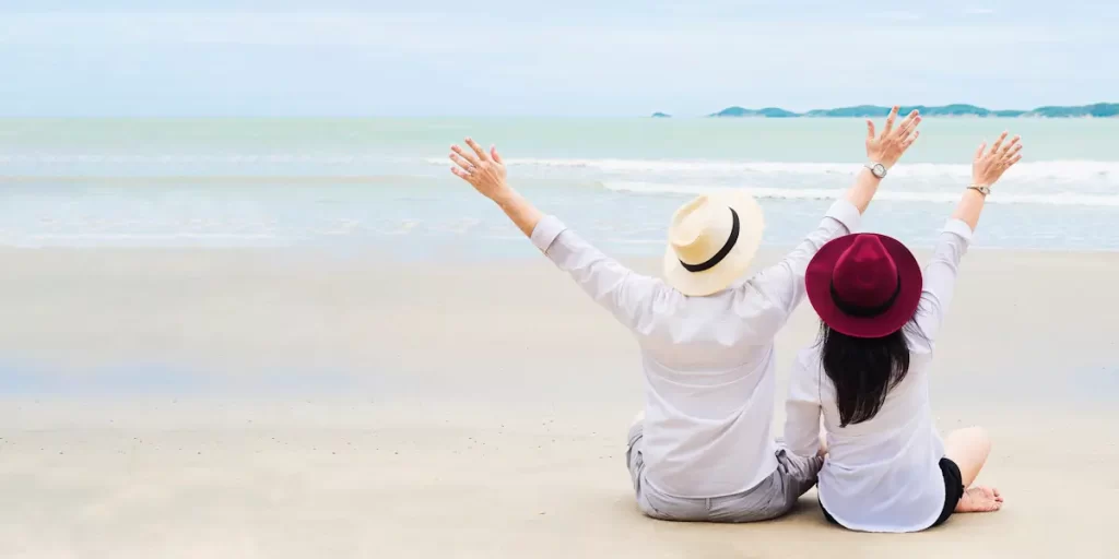 Paar ontspannen op strand met opgeheven handen met uitzicht op zee