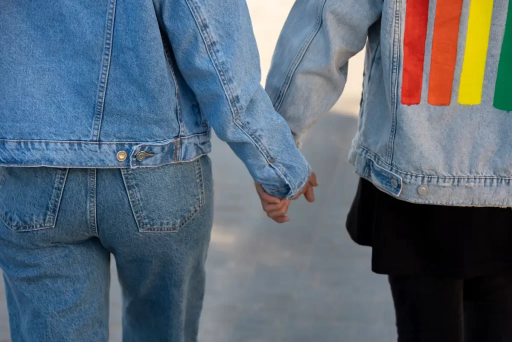 Two trans people holding hands, wearing denim jackets.