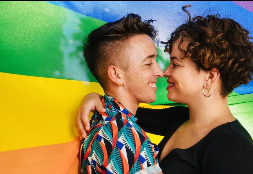 Two people smiling at each other in front of a rainbow flag